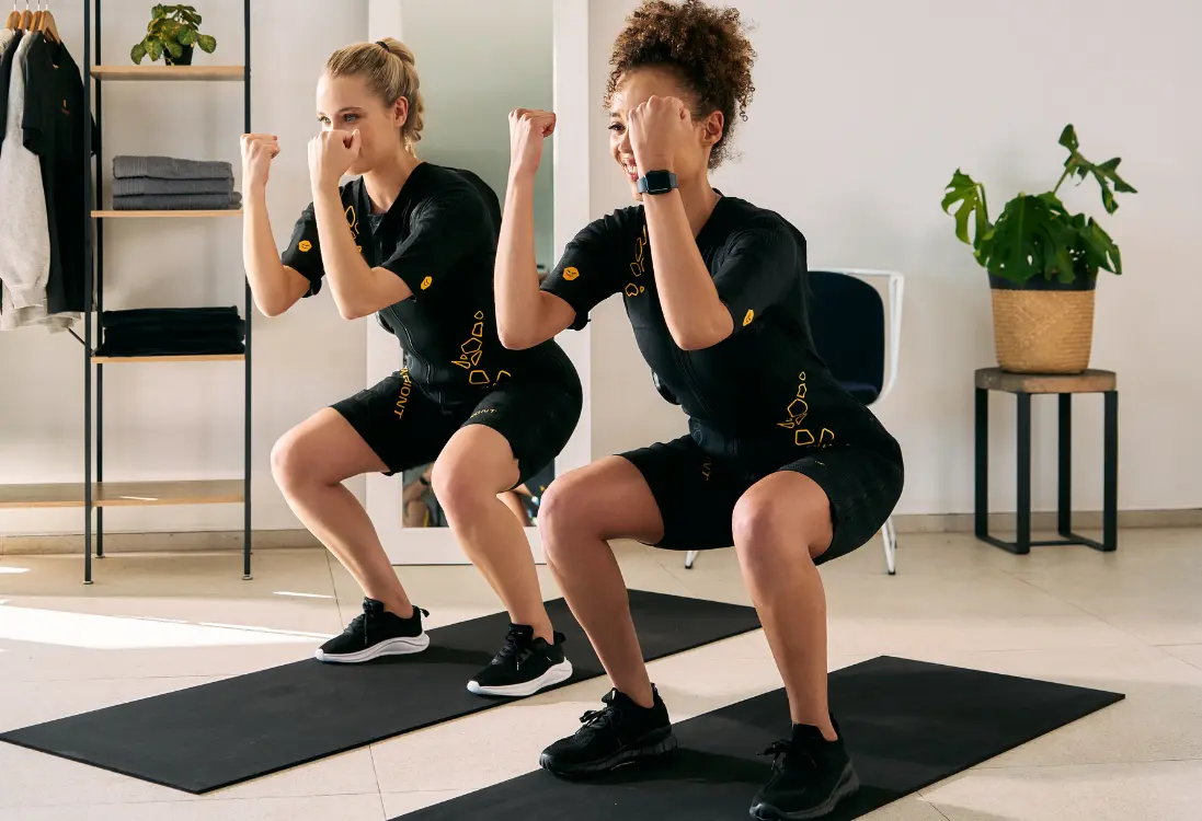 Fast results with EMS training in Prague Two women in EMS suits do squats and use EMS training in Prague to get quick results in a short time.
